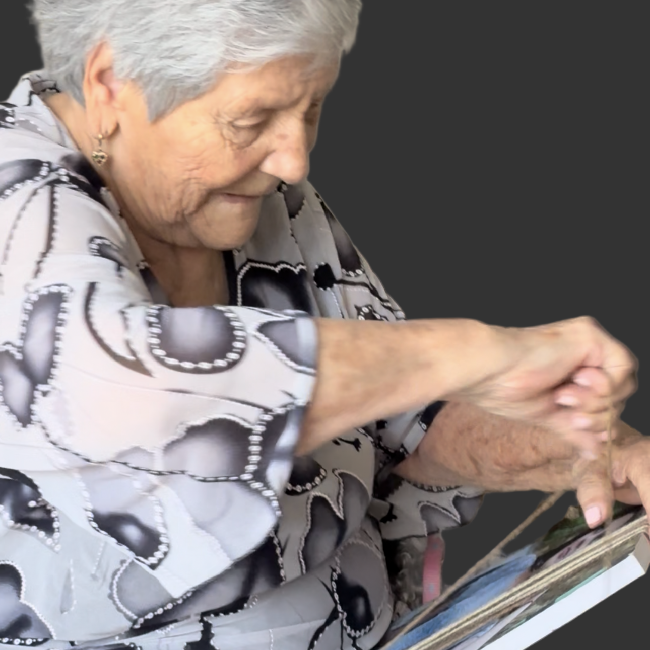 Senior woman sitting on a couch, knitting with a book of patterns.